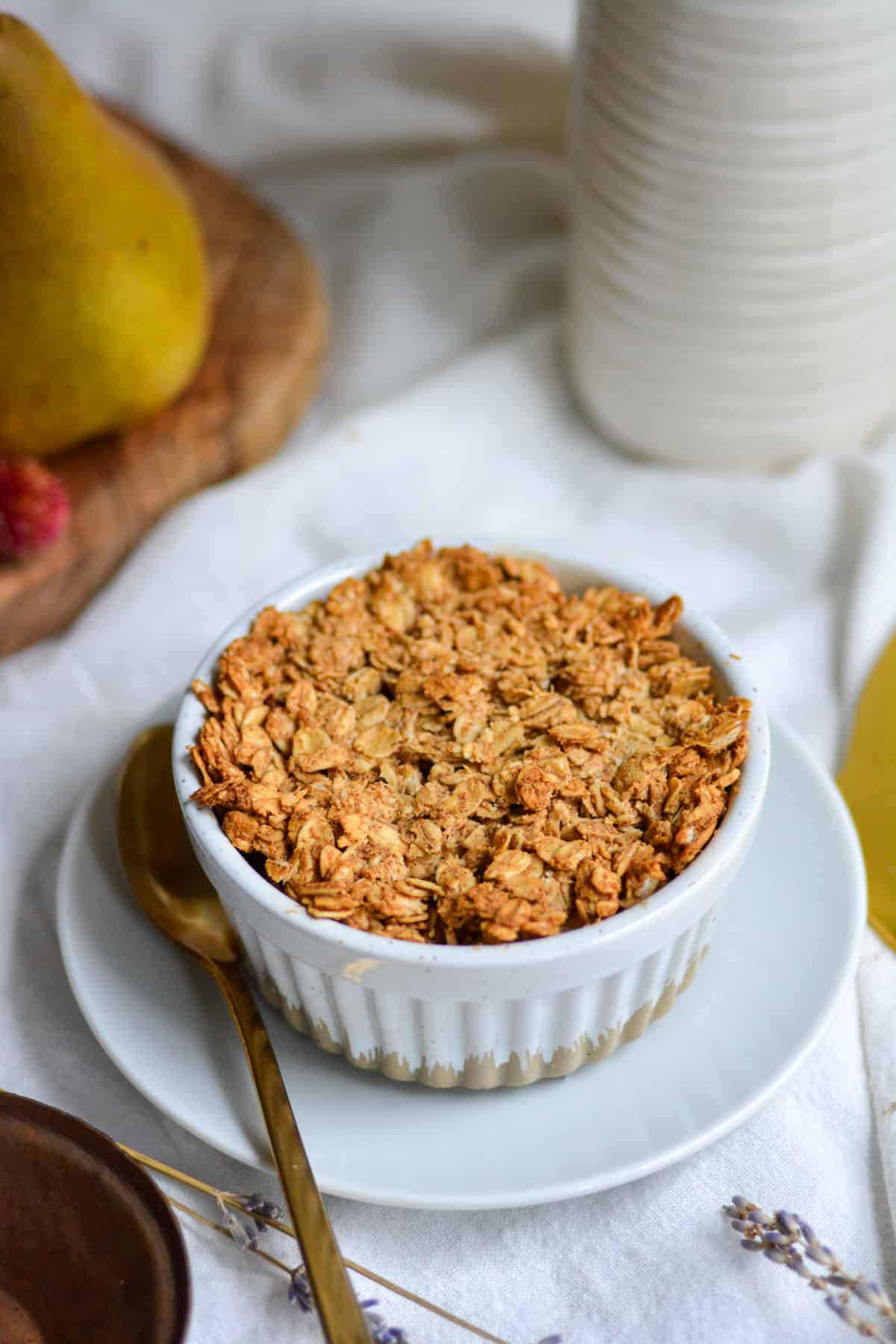 Vegan Gluten Free Pear Crumble in a ramekin on a white plate next to a gold fork.