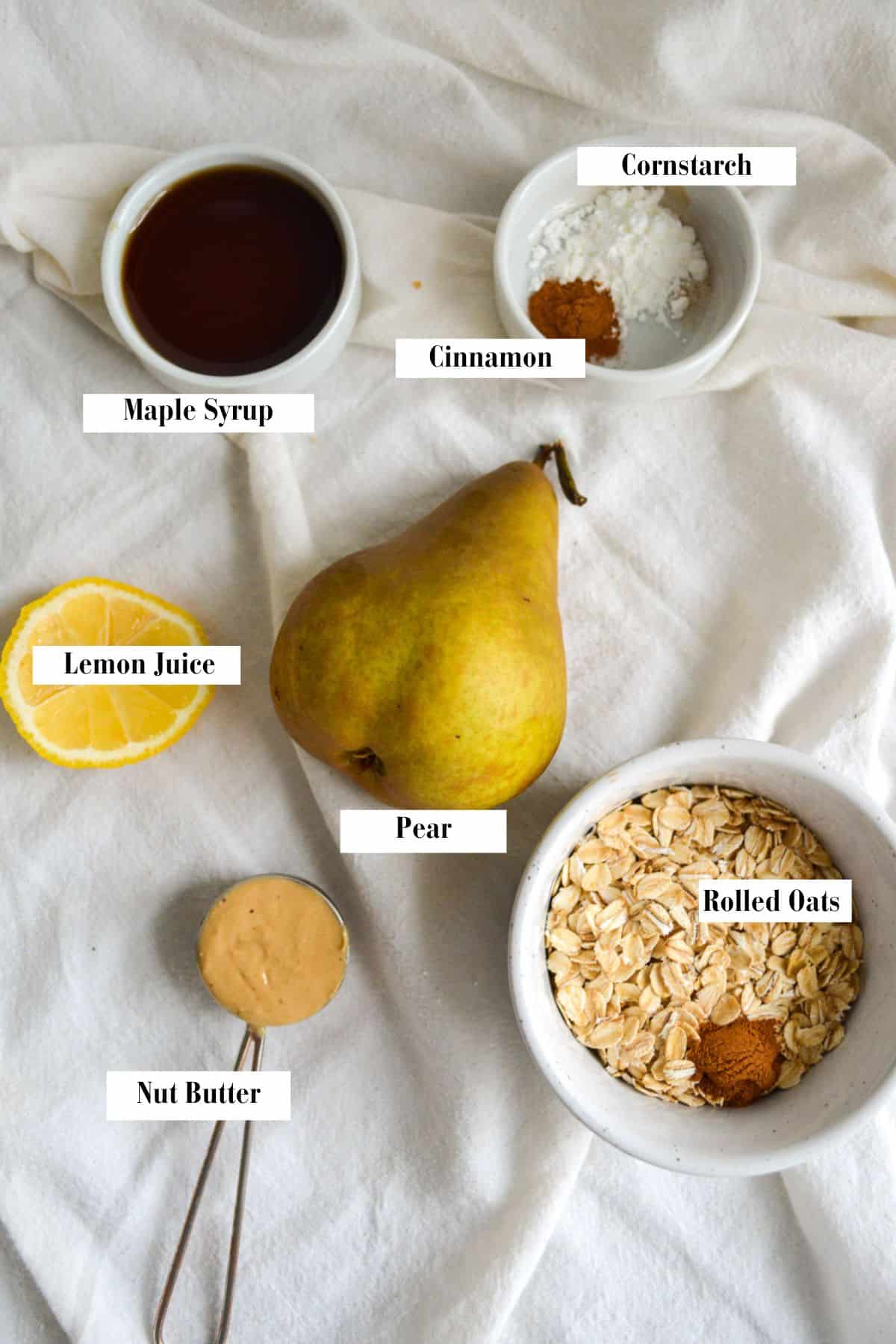 Overhead photo of a pear, rolled oats, cinnamon, a spoon of nut butter, a slice of lemon and maple syrup.