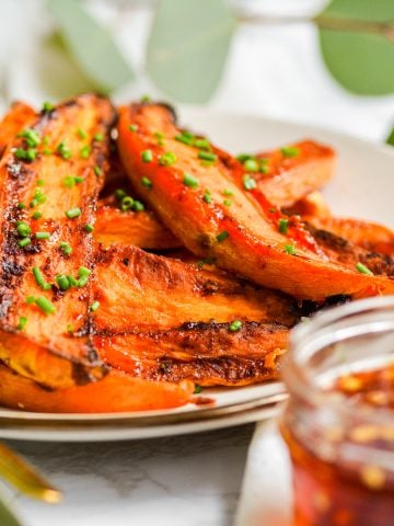 A plate with hot honey roasted sweet potato wedges on it with a container of hot honey in the foreground.