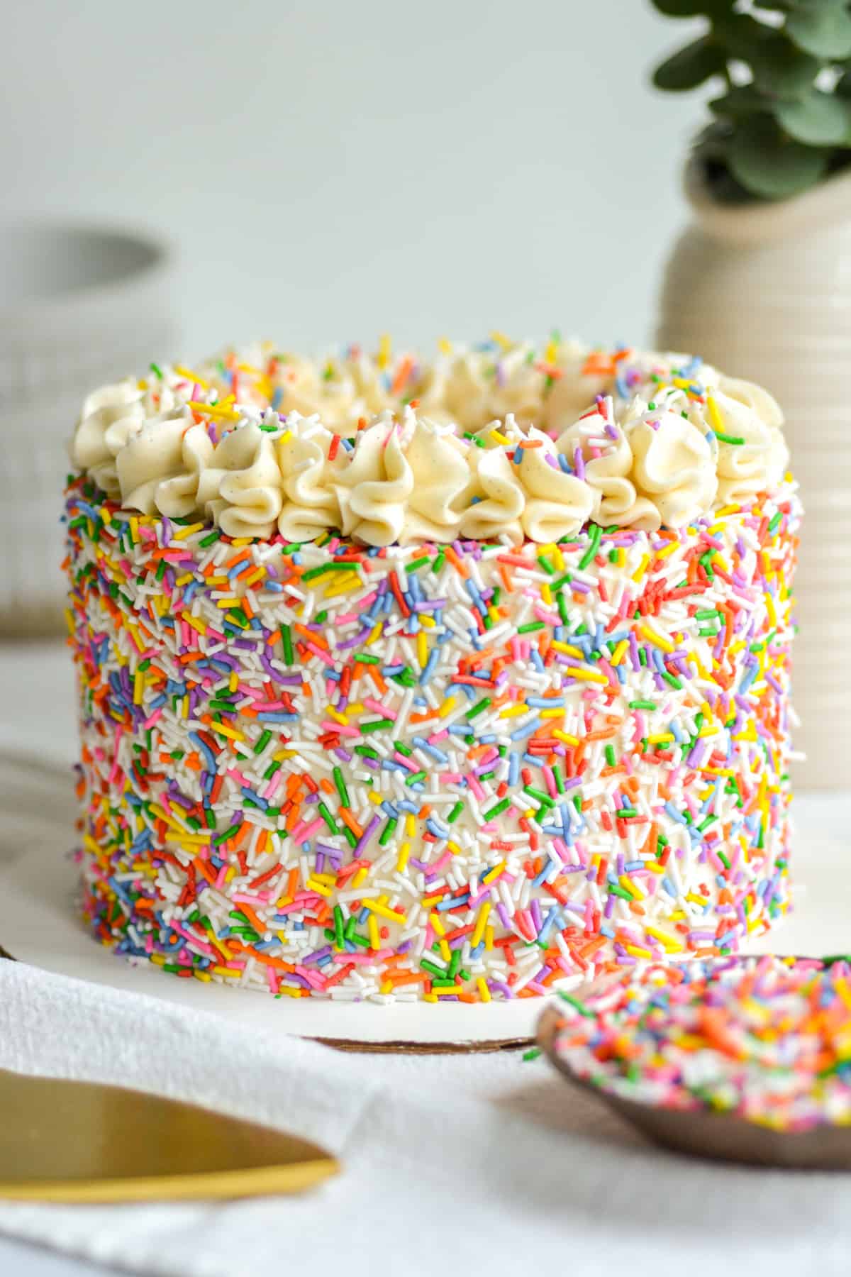 Eggless and Dairy Free Vegan Funfetti Cake covered in sprinkles on a white marble board.