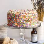 Vegan Funfetti Cake covered with sprinkles on a glass cake stand.