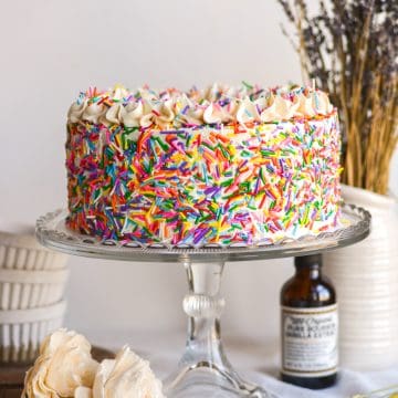 Vegan Funfetti Cake covered with sprinkles on a glass cake stand.