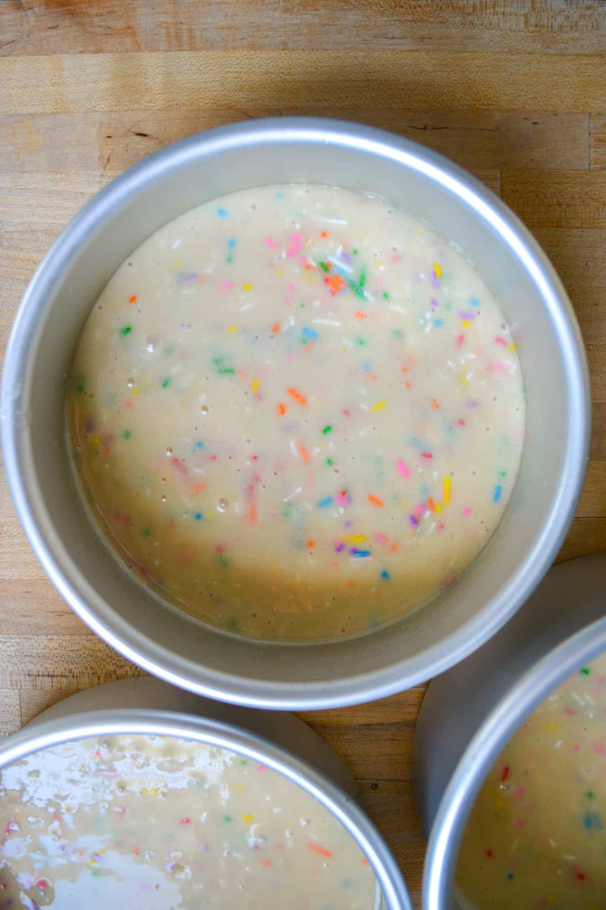 Cake batter with sprinkles mixed into it poured into a round cake pan.