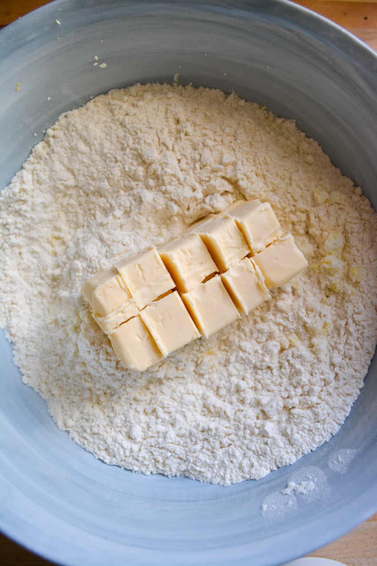 Cubed vegan butter added into the dry ingredients in a marble bowl.