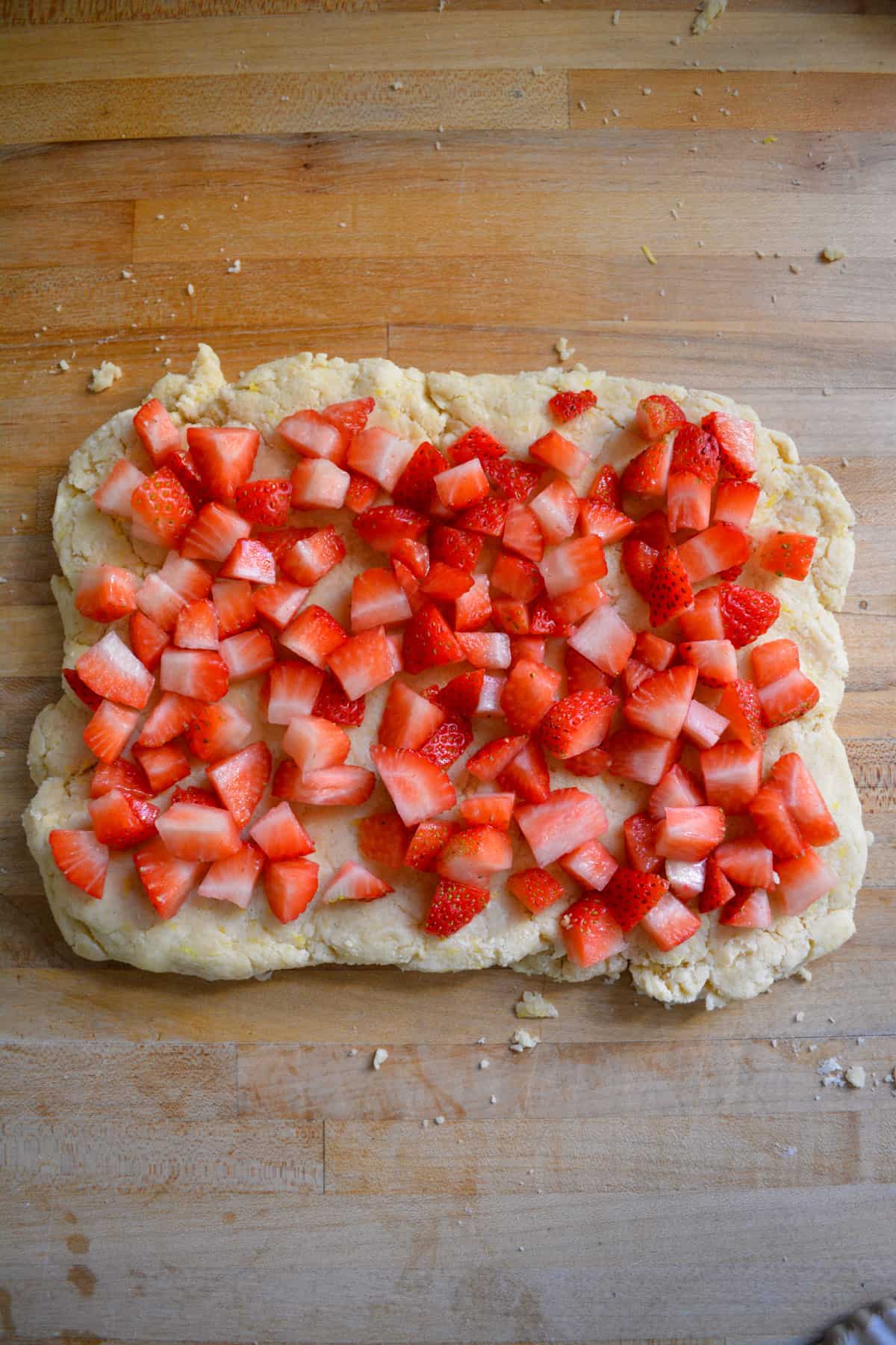 Scone dough patted nto a rectangle with chopped strawberries on top of it.