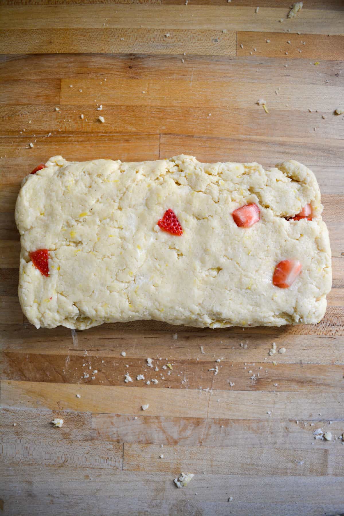 Vegan Lemon Strawberry Scone dough patted into a rectangle on a wooden surface.