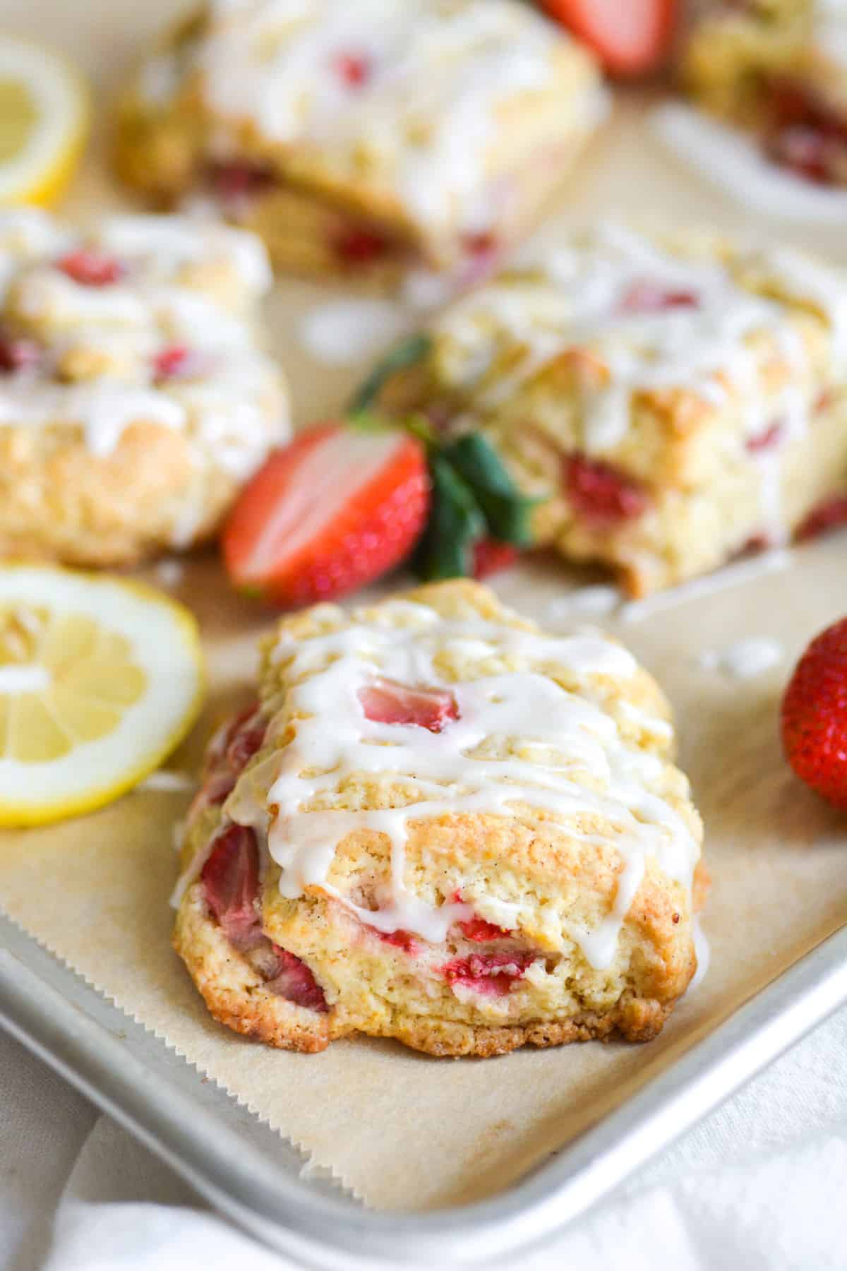 Vegan Lemon Strawberry Scones on a baking sheet with slices of lemon and strawberries in the scene.