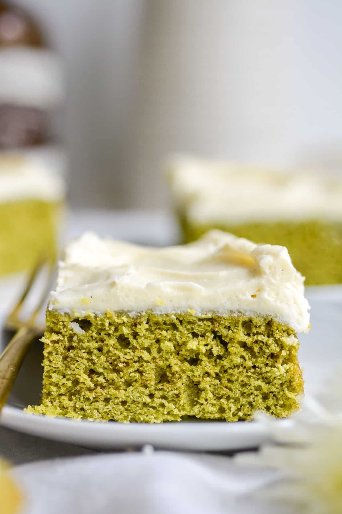 Straight on shot of vegan matcha cake on a white plate topped with vanilla frosting.