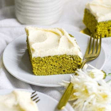 Vegan Matcha Cake on a white plate with a gold fork with white flowers in the foreground.