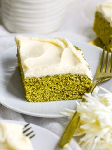 Vegan Matcha Cake on a white plate with a gold fork with white flowers in the foreground.