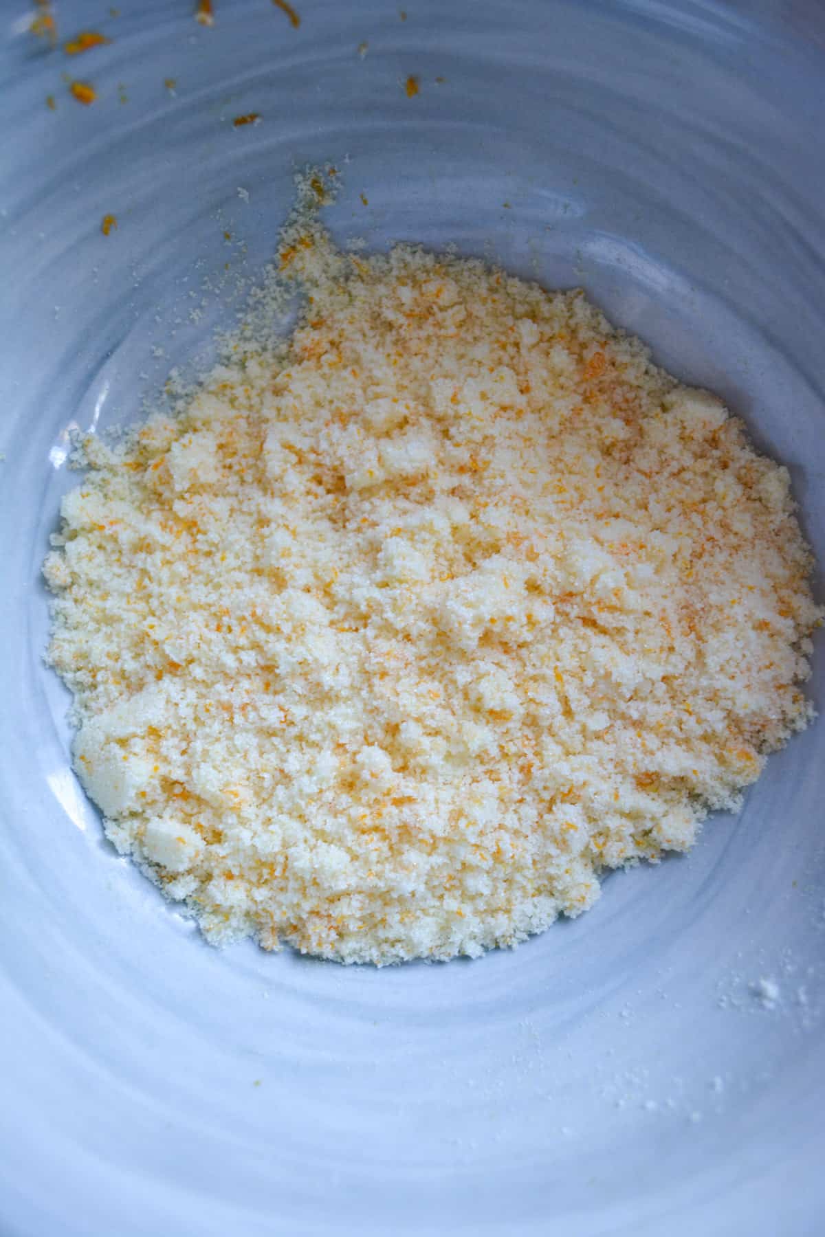 Orange zest rubbed together with granulated sugar in a marble bowl.