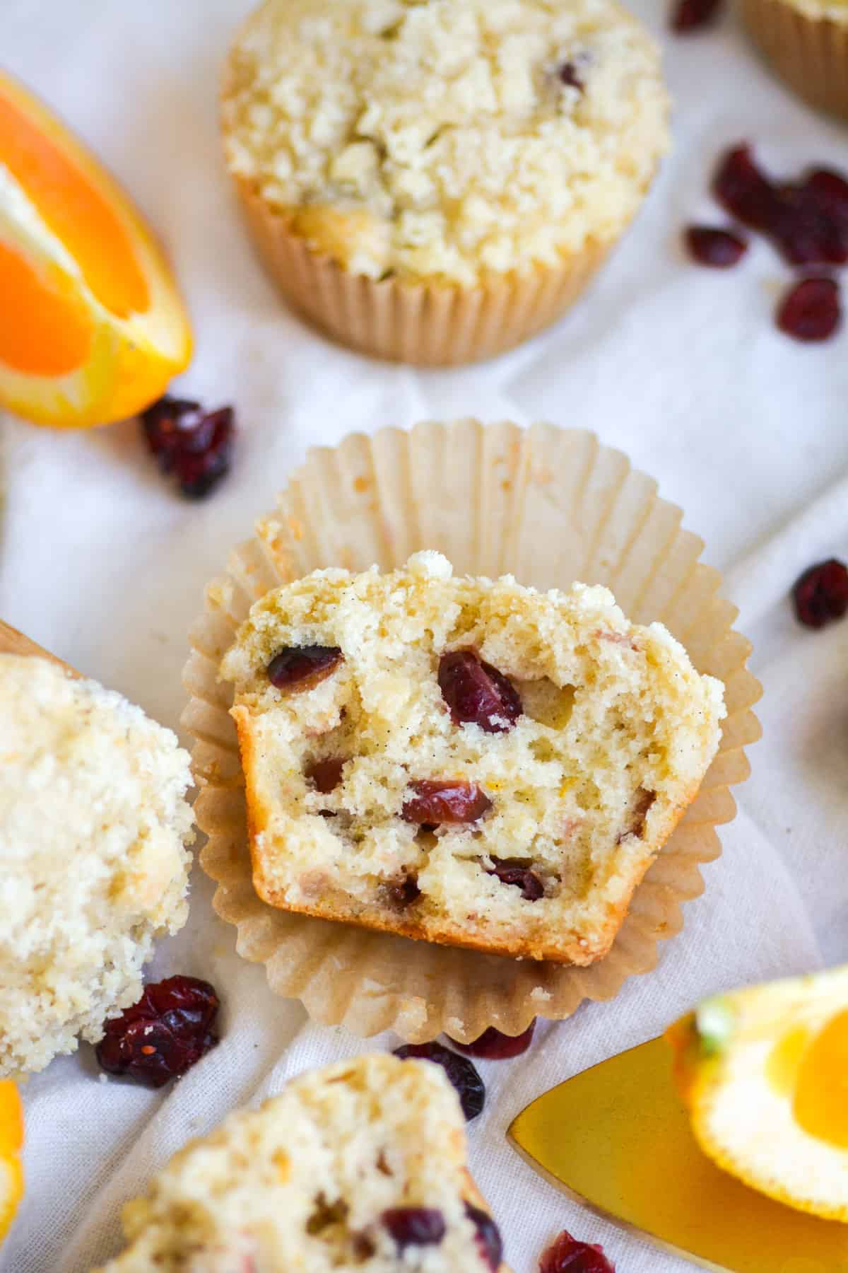 A Vegan Cranberry Orange Muffin broken in half and laying in the muffin liner.