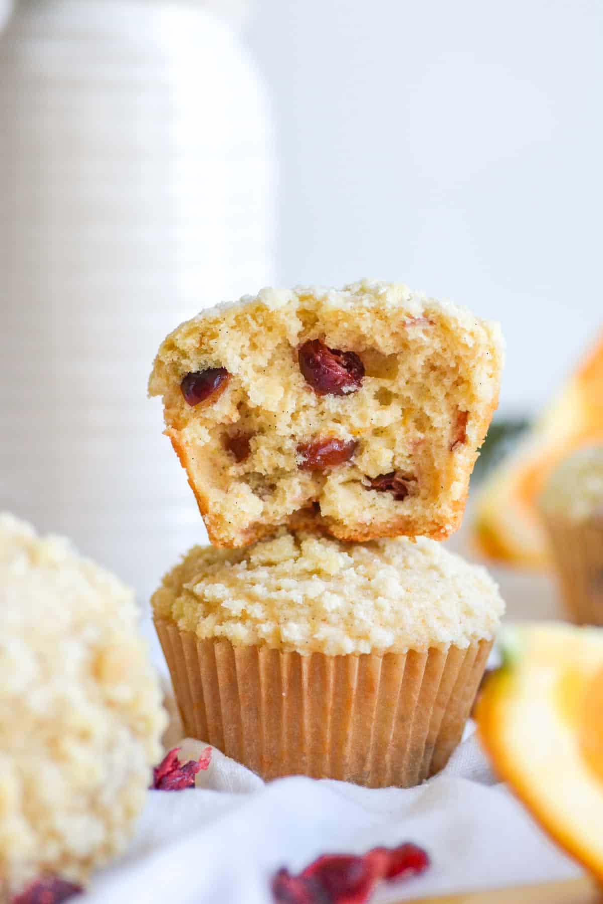 A muffin that is broken in half sitting on top of another Vegan Cranberry Orange Muffin.