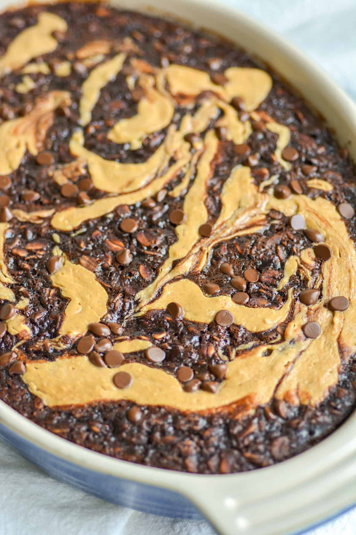 Chocolate Baked Oatmeal with peanut butter swirl in a baking dish on a white cloth.