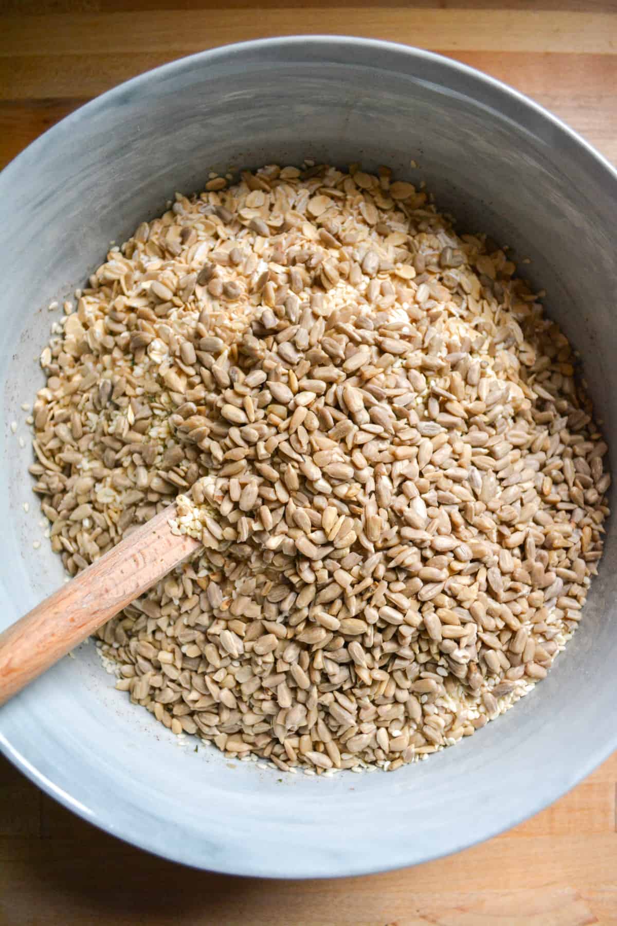 Rolled oats and seeds added into the mixing bowl with a spatula in it.