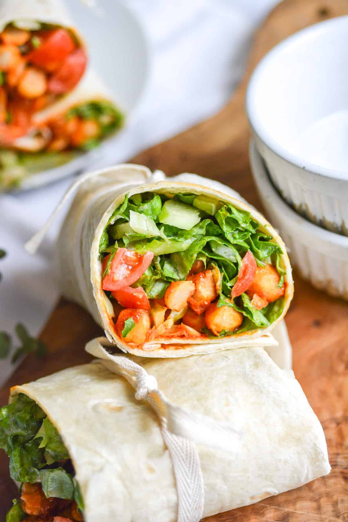 A Vegan Buffalo Chickpea Wrap cut in half to show the inside, resting on another wrap.