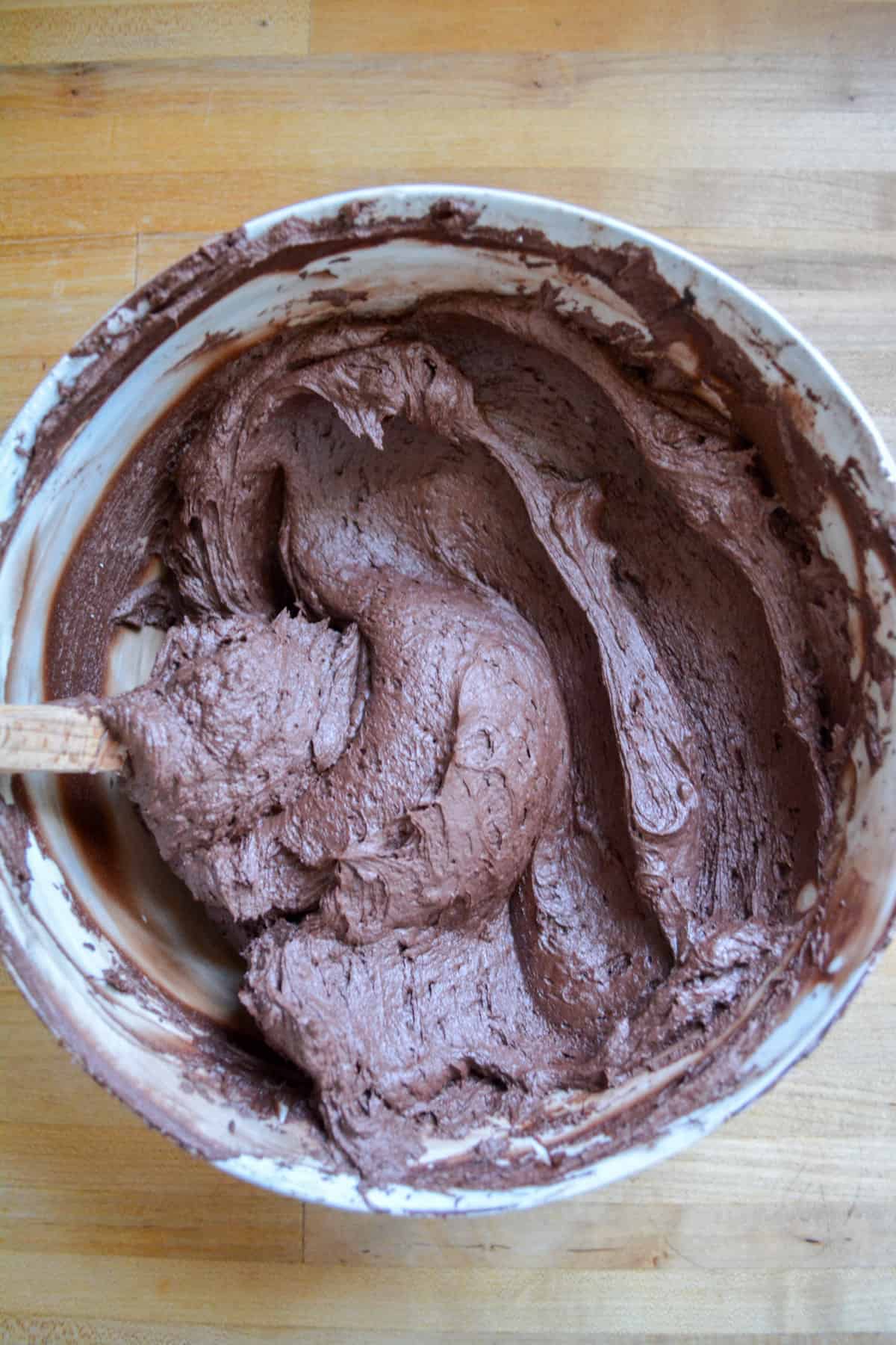 The finished Vegan Chocolate Buttercream Frosting in a marble bowl with a spatula in it.