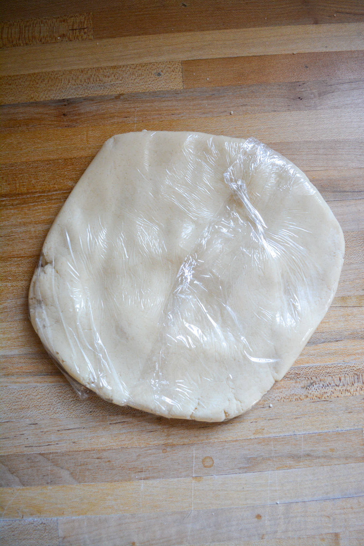 A disc of dairy-free sugar cookie dough wrapped with plastic wrap.