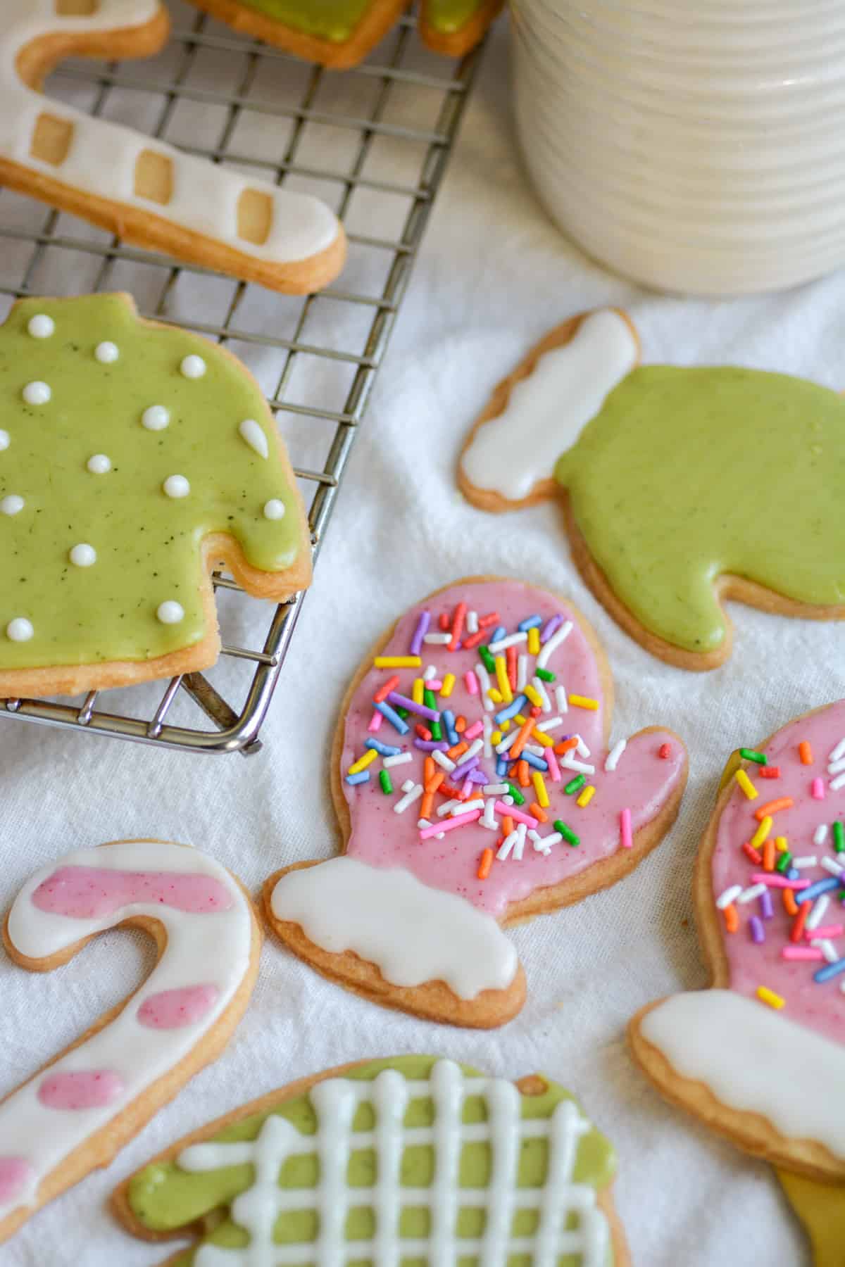 Vegan Cut-Out Sugar Cookies decorated with white, pink and green icing on a white cloth.