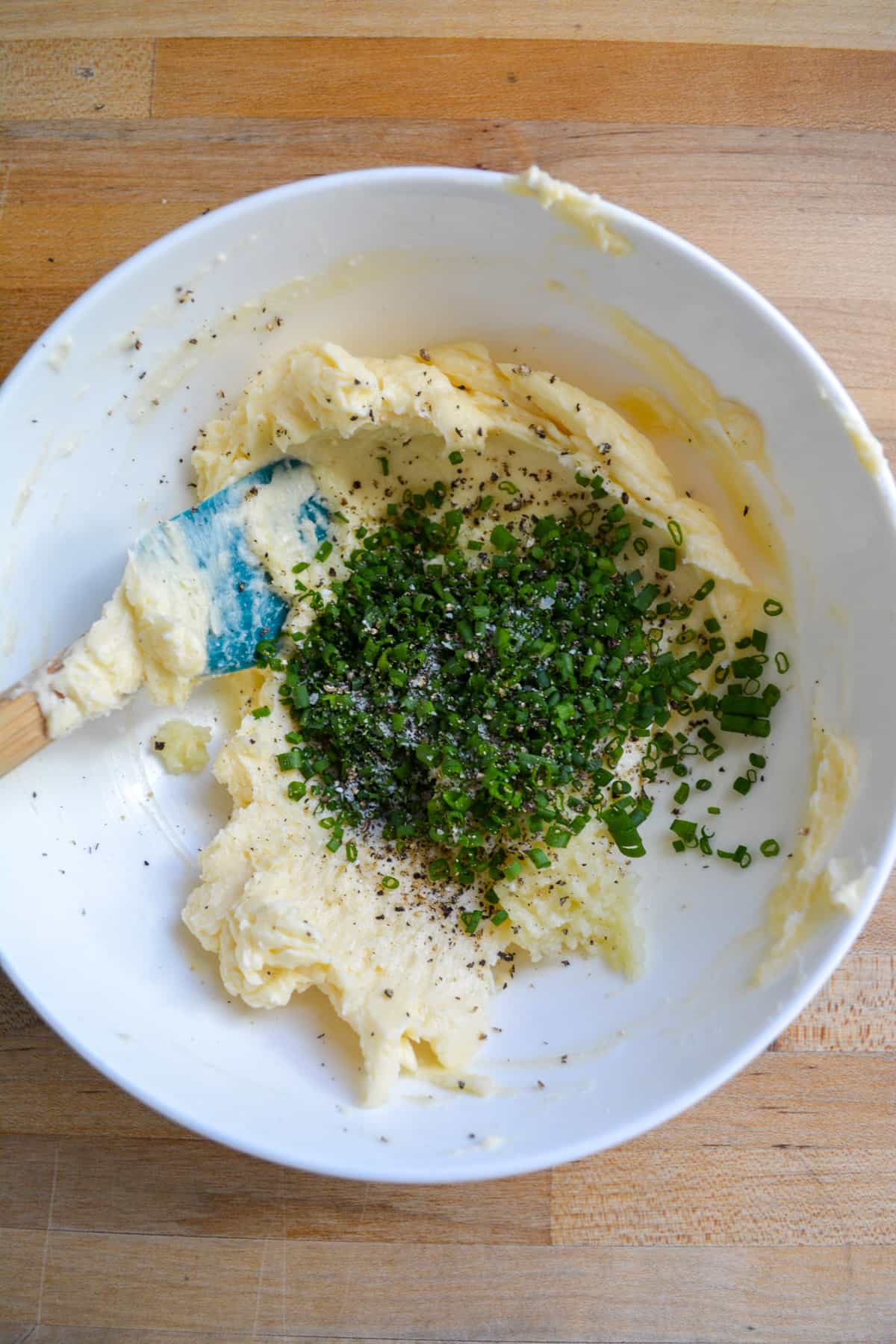 A white bowl with dairy-free butter, garlic and chives in it.