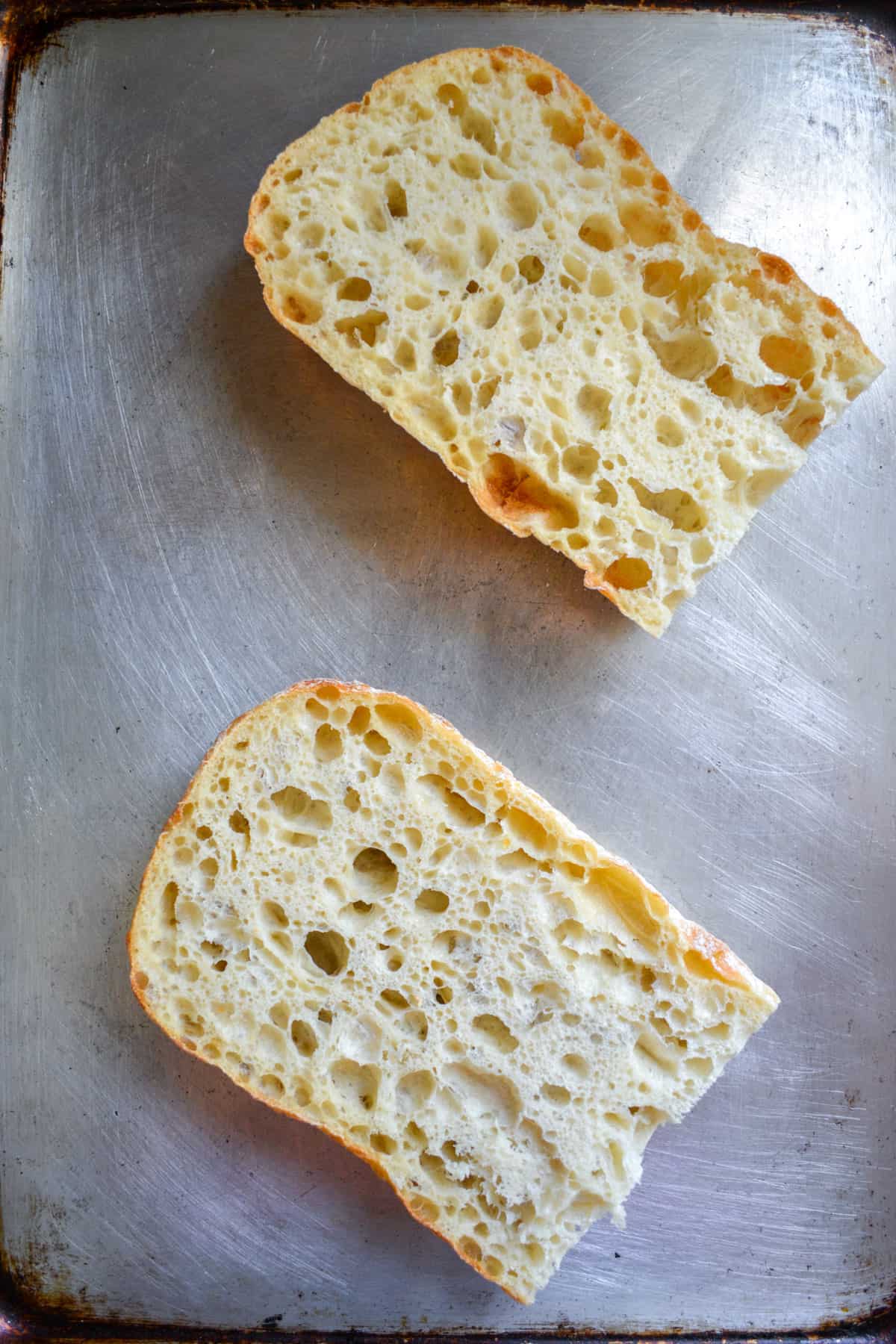 A loaf of ciabatta sliced in half on a baking sheet.