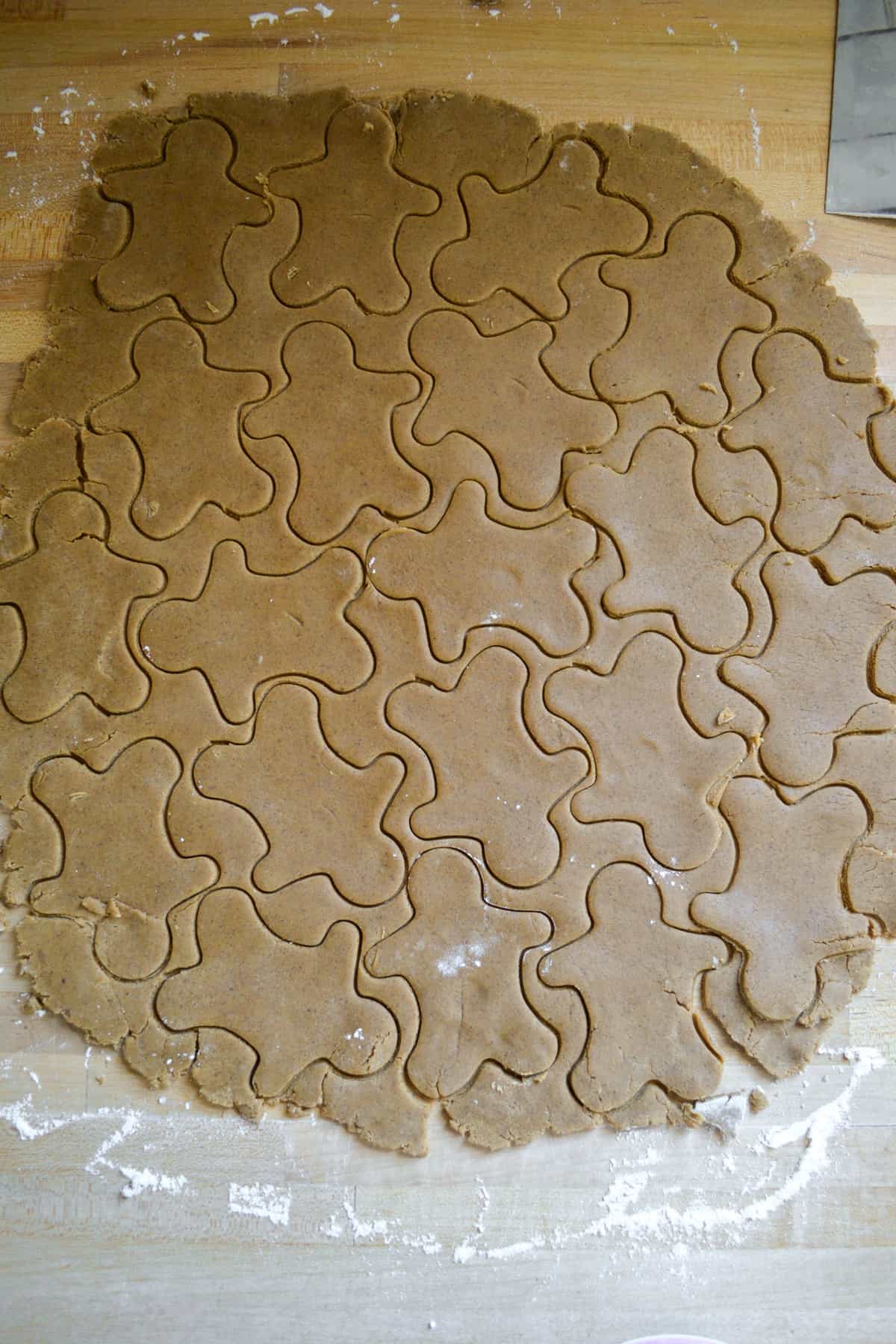 Gingerbread dough rolled out on a wooden surface with cookies cut out of it.