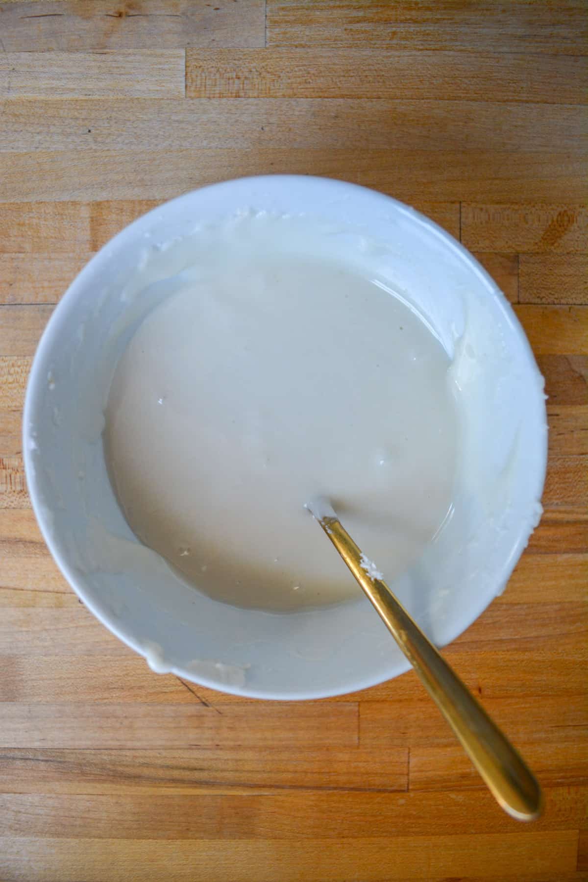 Vegan royal icing in a white bowl with a gold spoon.