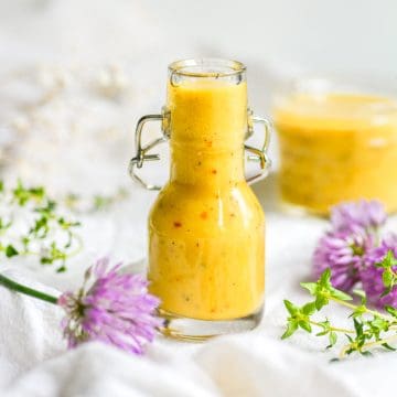 Vegan Honey Mustard Dressing in a small jar on a white cloth with purple flowers in the foreground.