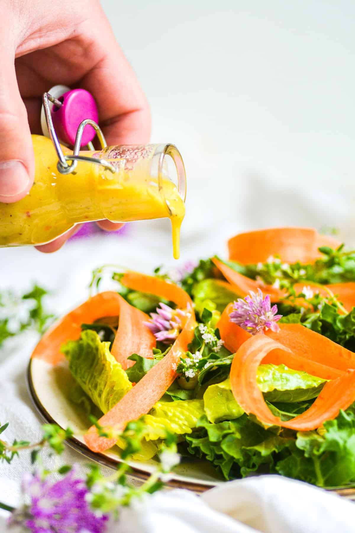 Pouring Vegan Honey Mustard Dressing onto a green salad on a plate.