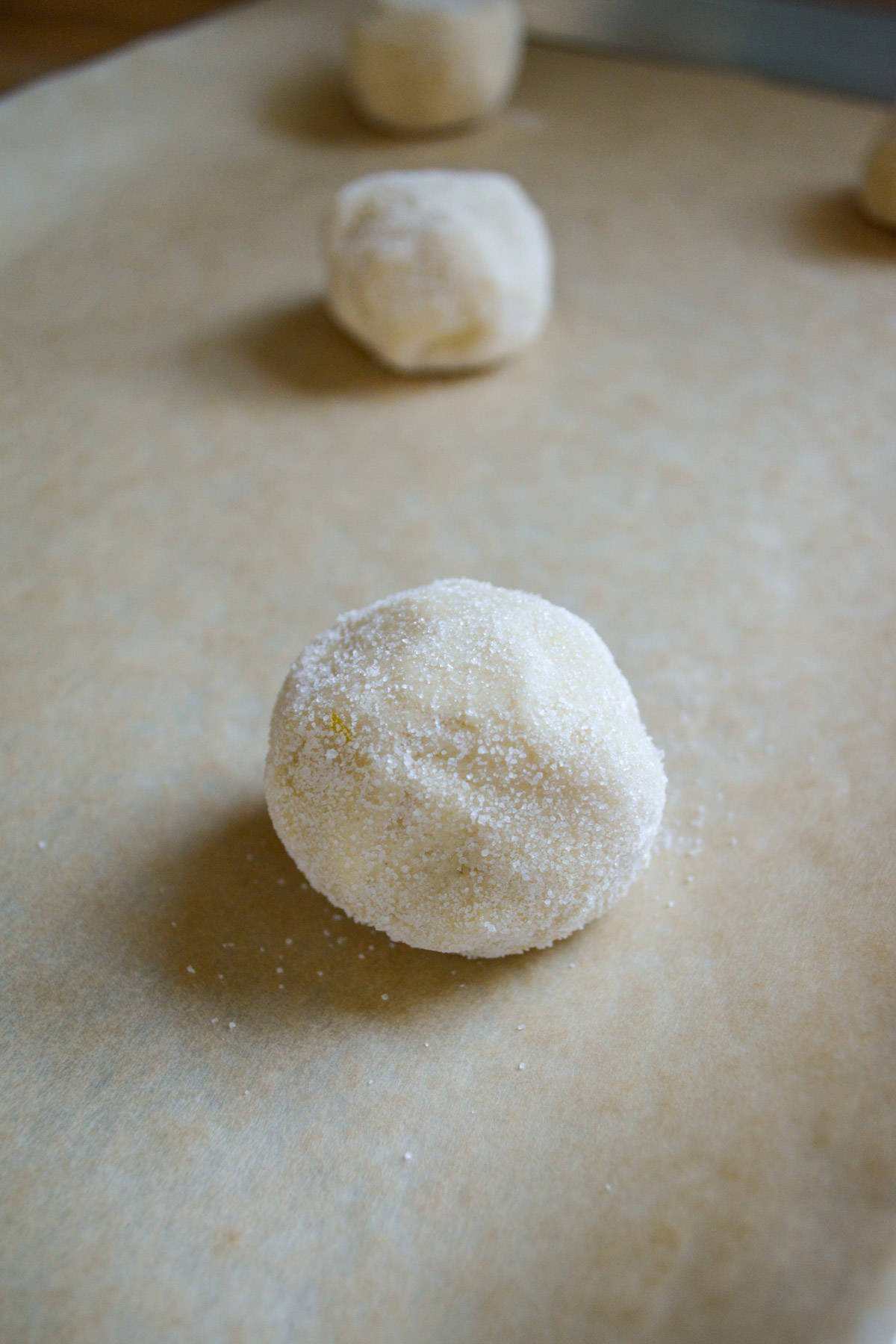 Dairy-Free lemon cookie dough ball on a parchment lined baking sheet.