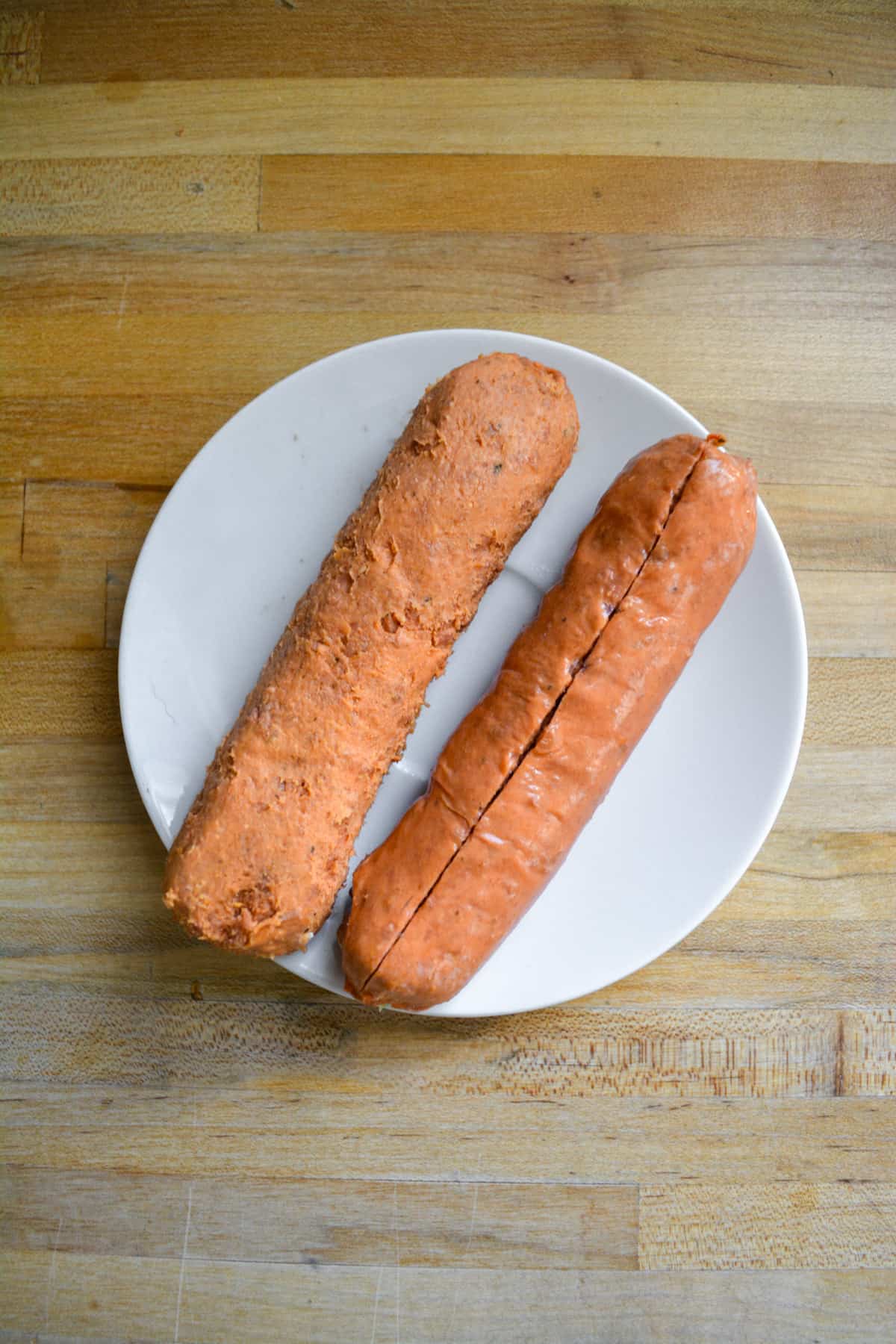 Two vegan Sausages on a small plate, removing the casing.