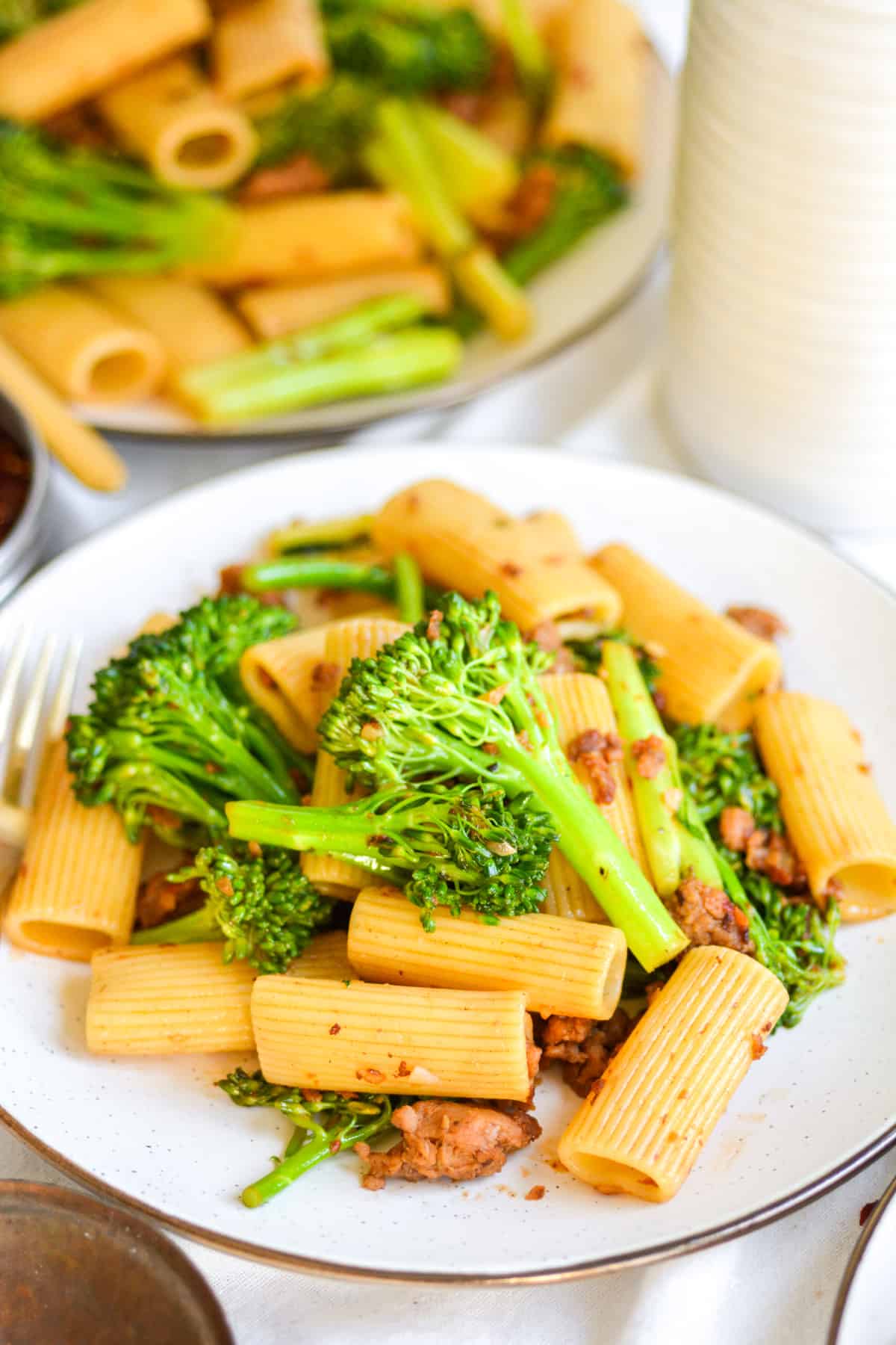 Vegan Sausage Pasta with broccolini on a beige plate with a gold fork.