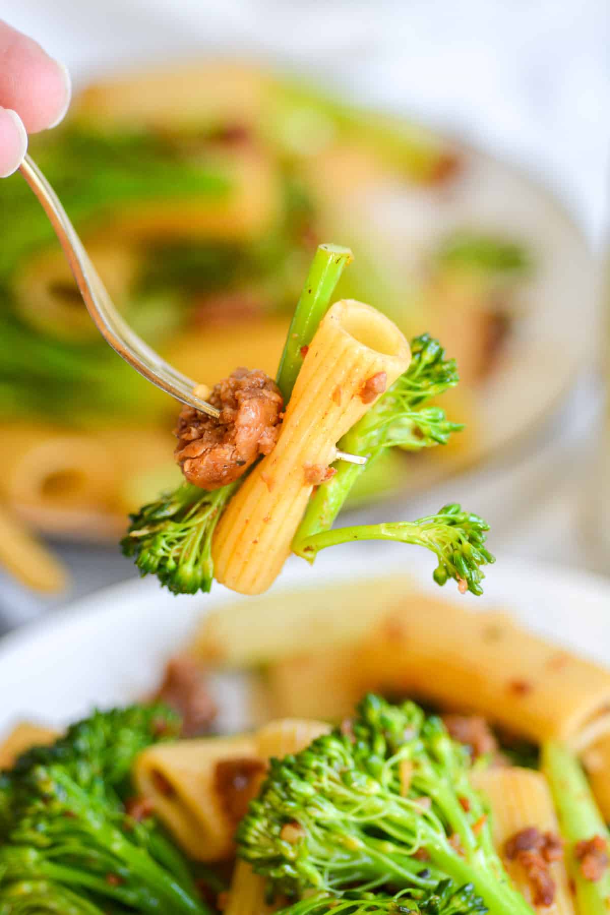 Gold fork with a bite of vegan sausage pasta with broccolini on it.