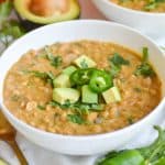 A bowl of vegan and vegetarian white bean chili topped with cilantro and avocado chunks.