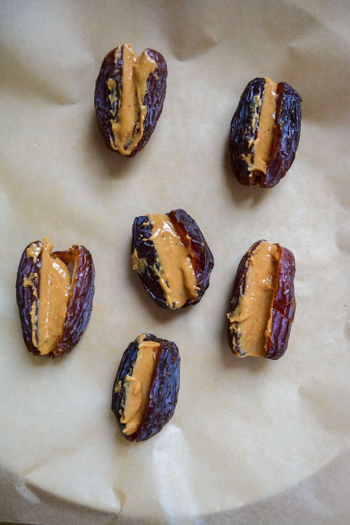 Peanut butter stuffed in the middle of the dates on a parchment lined plate.