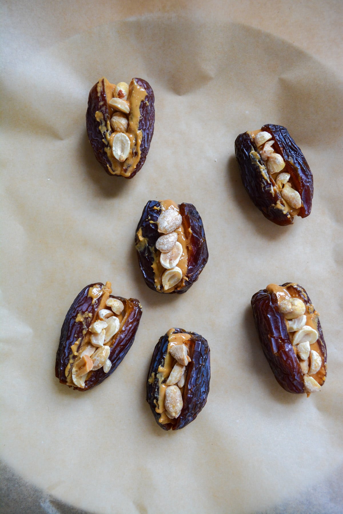 Peanut butter stuffed dates topped with peanuts on a parchment lined plate.