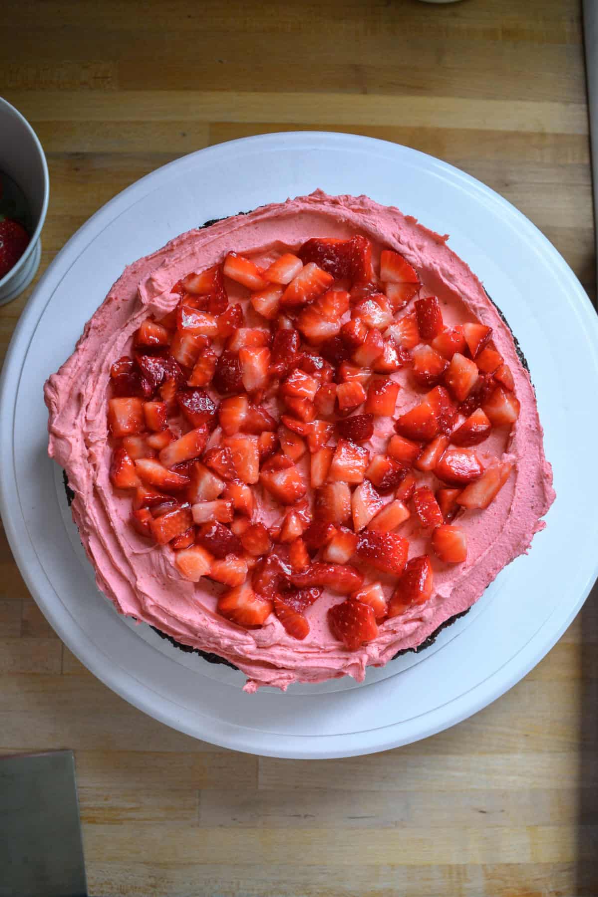 A chocolate cake layer with strawberry frosting and chopped strawberries on top.