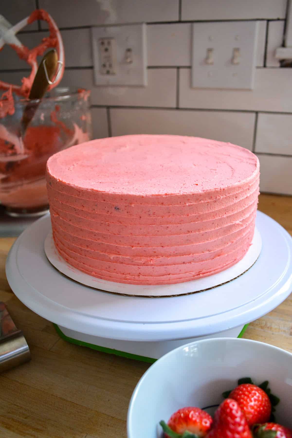 A cake on a turntable frosted with strawberry frosting.