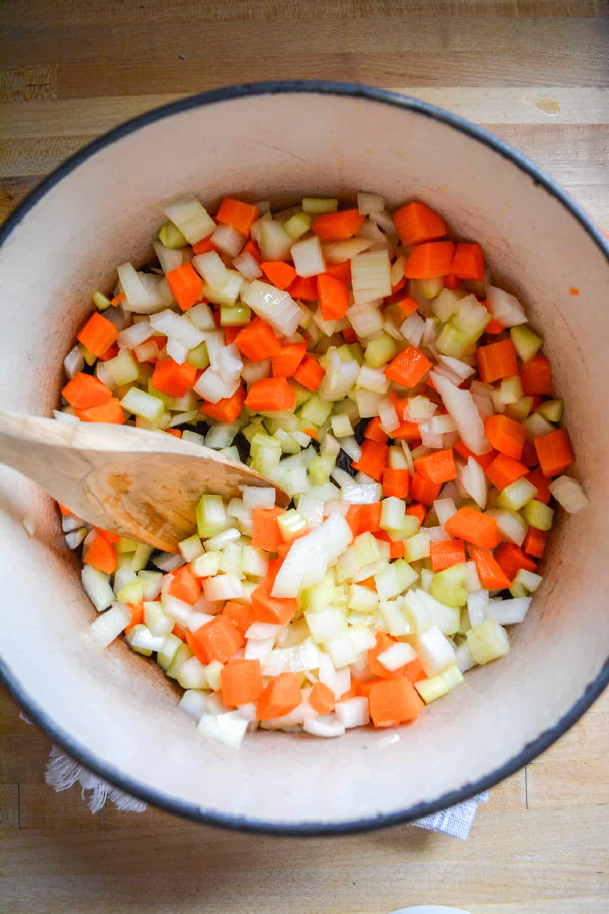 Diced onion, carrot and celert in a dutch oven with a wooden spoon.