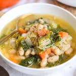 White Bean and Escarole Soup in a white bowl with a gold spoon.