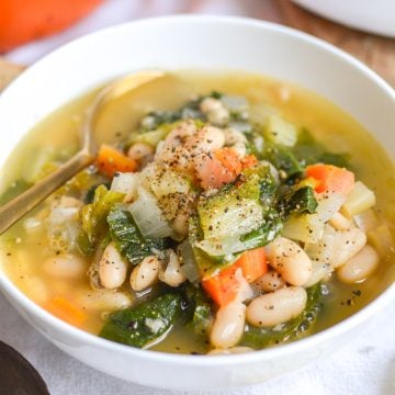 White Bean and Escarole Soup in a white bowl with a gold spoon.