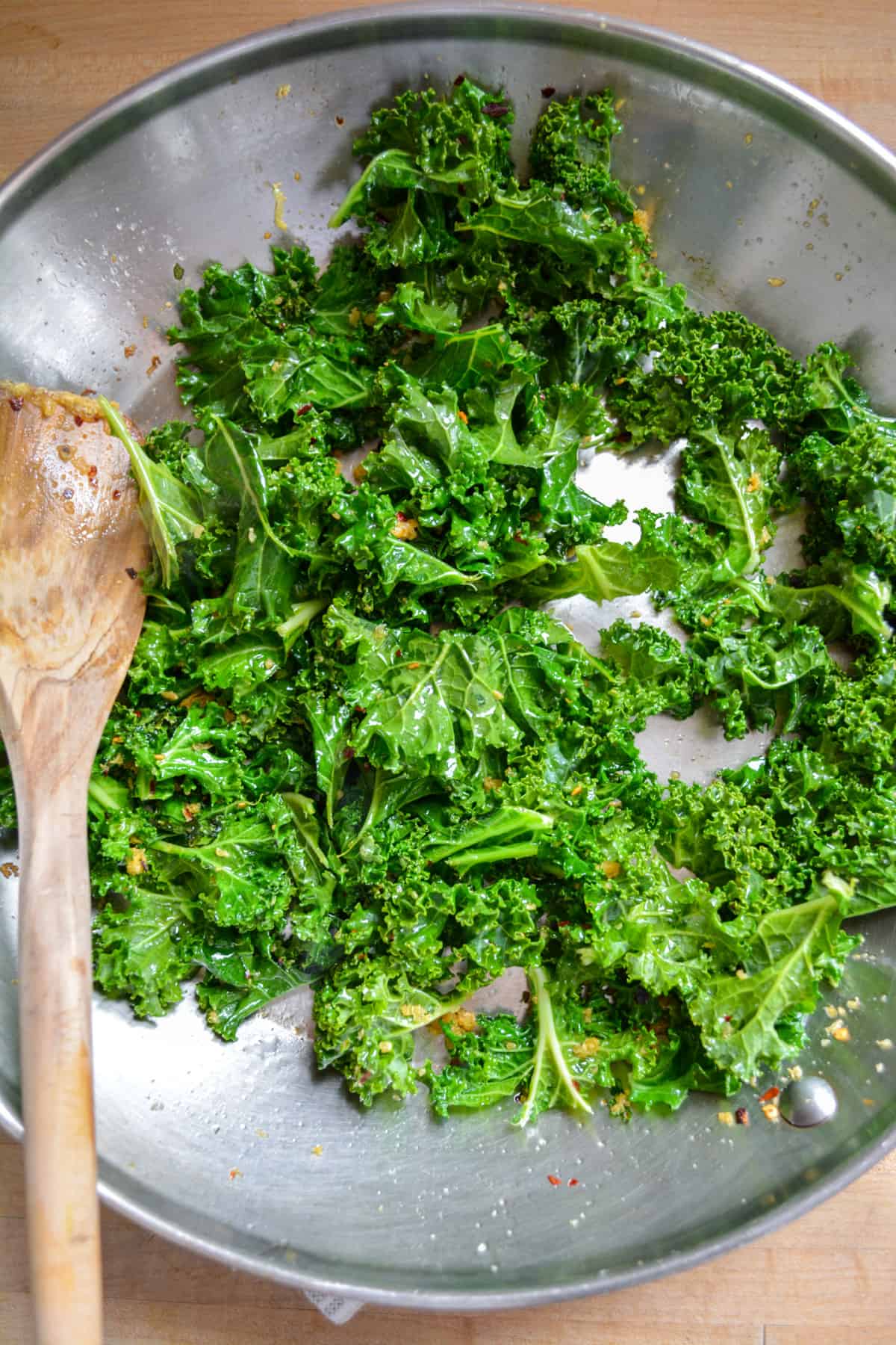 Wilted kale in a stainless sleet skillet with a wooden spoon off to the left.