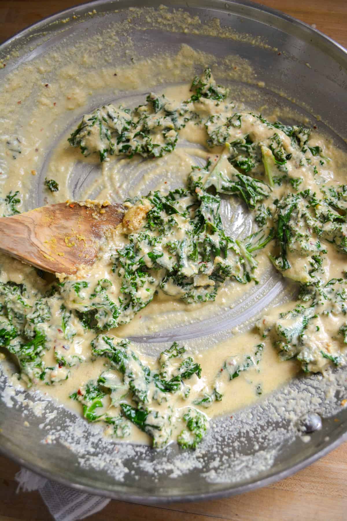 The creamy tahini sauce all stirred up with the kale in a skillet.