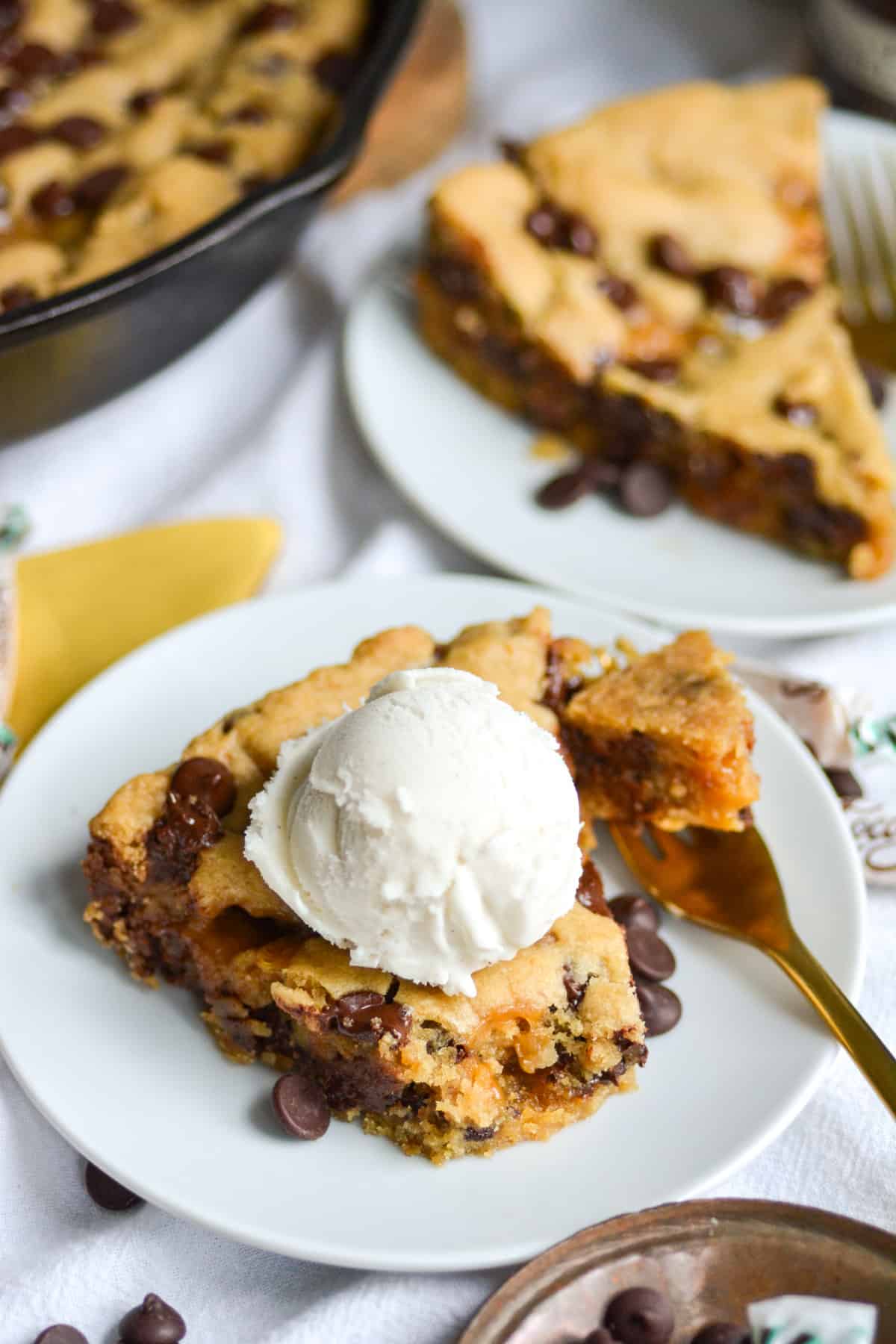 Vegan Salted Caramel Chocolate Chip Cookie Skillet slice on a small white plate topped with vegan vanilla ice cream.