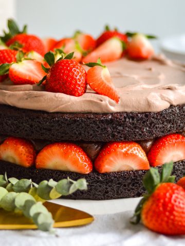 Vegan Chocolate Strawberry Fudge Cake on a white cloth with strawberries in the foreground.
