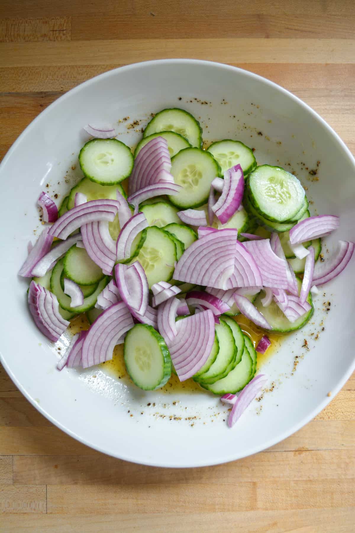 Sliced cucumber and sliced red onion added into the bowl with the salad dressing.