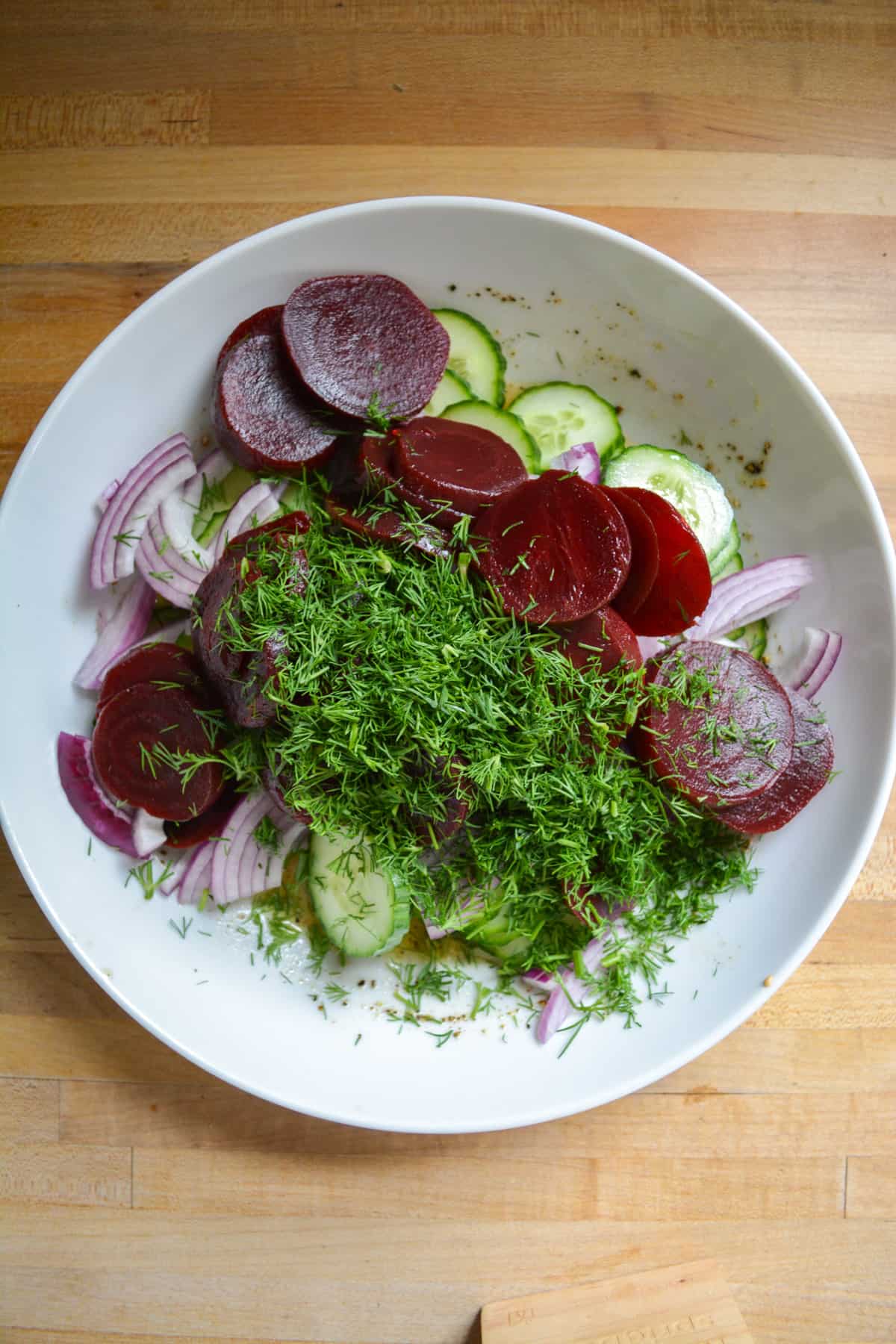Sliced beets and chopped dill added into the white bowl with the cucumber and red onion.