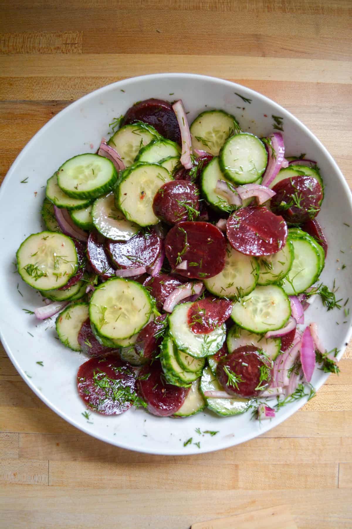 Beet cucumber salad all tossed together in a white bowl.