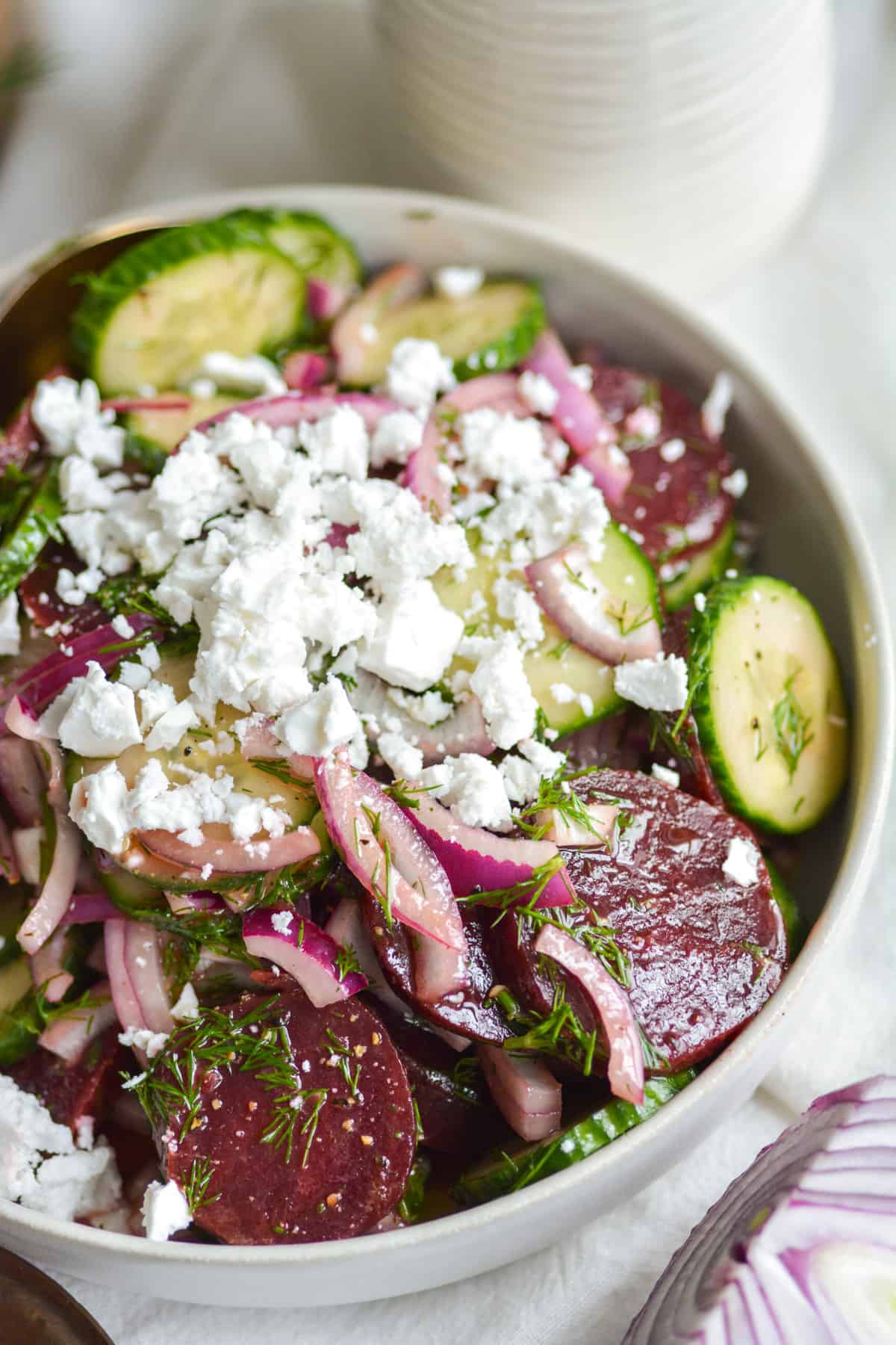 Close up of beetroot cucumber salad topped with vegan feta in a white bowl.