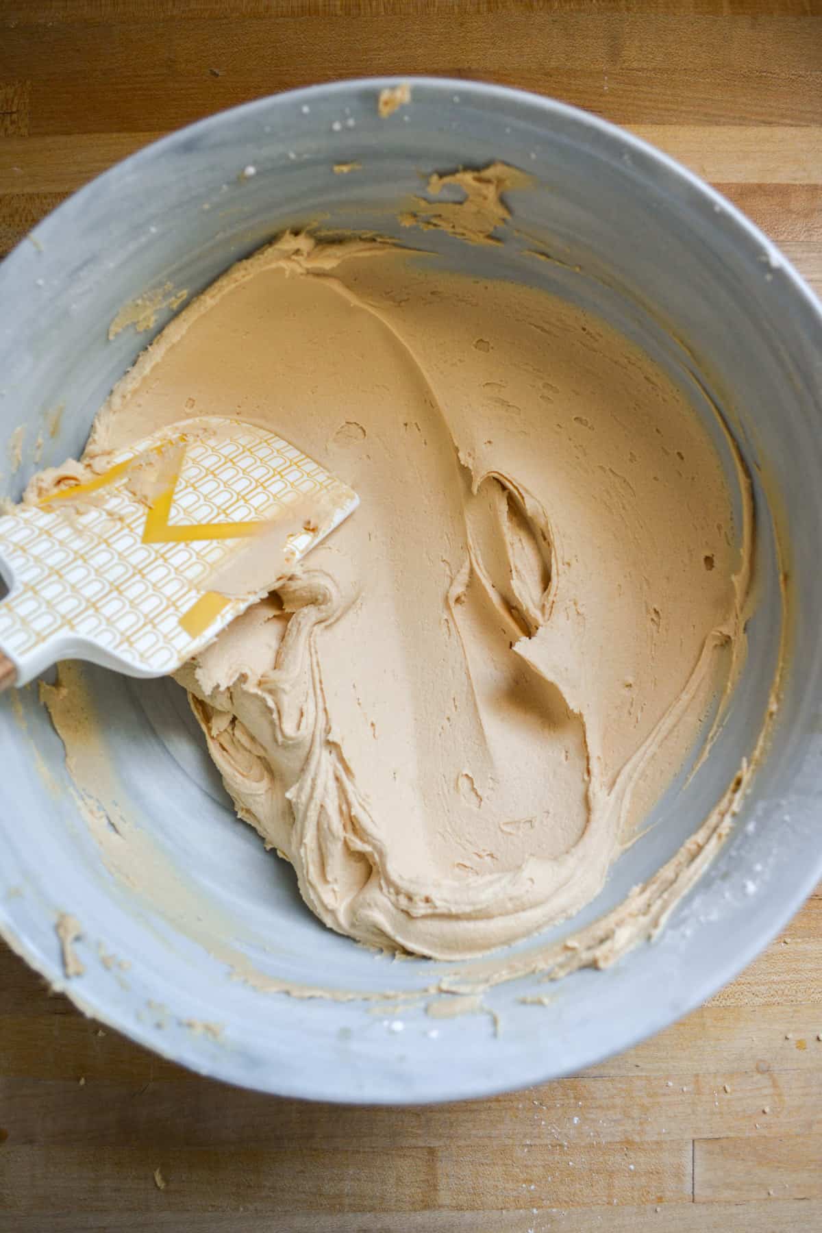 Biscoff Buttercream Frosting in a mixing bowl with a rubber spatula to the left.